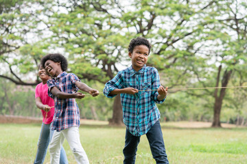 Happy African American childrens playing rope tug of war in the park, Education outdoor concept
