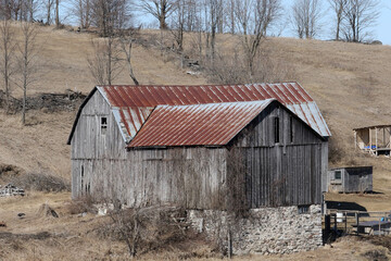 Old barn with rusted roof built on a slope on a farm in Ontario in early spring before grass grows
