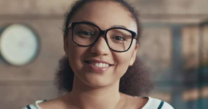 Close up portrait of young multiethnic ethnic girl in glasses standing in modern office and looking at camera smiling.
