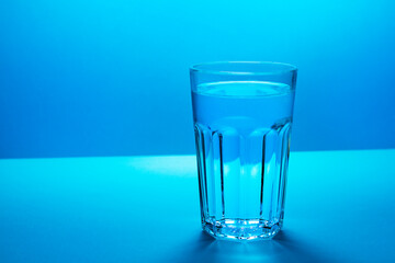 A glass with water in a blue colors background.