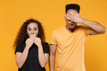 Young couple two sad friends family shocked african man woman together in black t-shirt cover mouth with hand put arm on face facepalm epic fail gesture isolated on yellow background studio portrait.