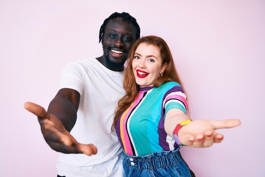 Interracial couple wearing casual clothes smiling cheerful offering palm hand giving assistance and acceptance.