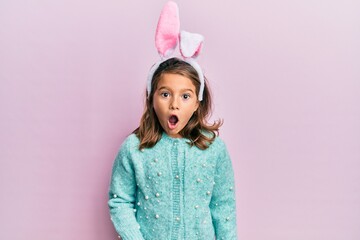Little beautiful girl wearing cute easter bunny ears afraid and shocked with surprise expression,...