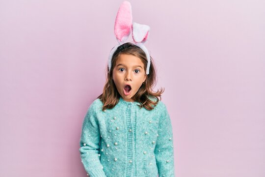 Little beautiful girl wearing cute easter bunny ears afraid and shocked with surprise expression, fear and excited face.