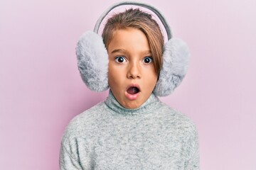 Little beautiful girl wearing fluffy earmuff afraid and shocked with surprise and amazed...