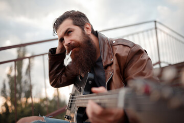 a man with a long red beard and gray hair in a brown leather jacket holds an electric guitar in his...