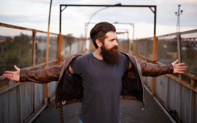A male rocker with a long beard and mustache in a brown leather jacket raised his arms to the sides...
