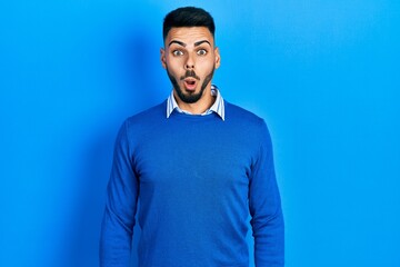 Obraz premium Young hispanic man with beard wearing casual blue sweater afraid and shocked with surprise and amazed expression, fear and excited face.