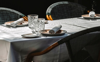 Two glasses stand out on a restaurant table set for three on a white tablecloth