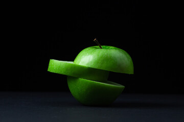 Green apple on a dark background. A cut green apple on a black background. Healthy food