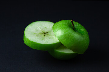 Green apple on a dark background. A cut green apple on a black background. Healthy food