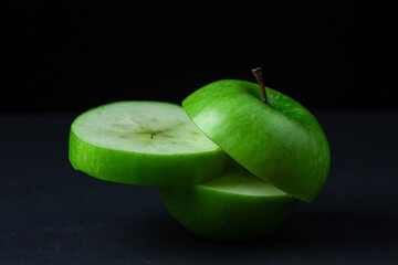 Green apple on a dark background. A cut green apple on a black background. Healthy food