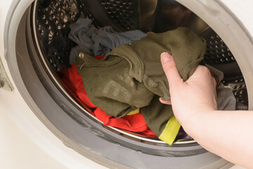 A woman's hand puts dirty baby clothes in the washing machine.Concept washing dirty spots, the best means of cleaning kids clothes.