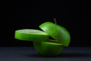 Green apple on a dark background. A cut green apple on a black background. Healthy food