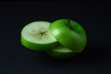 Green apple on a dark background. A cut green apple on a black background. Healthy food