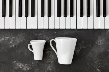 Keyboard of a piano with one small and one bigh white mugs in front of it