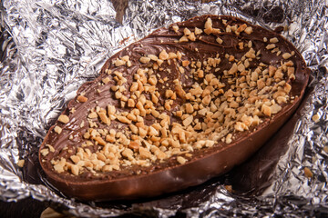 Stuffed chocolate easter egg with peanut and caramel on an aluminium foil on a wooden table with lots of peanuts around.