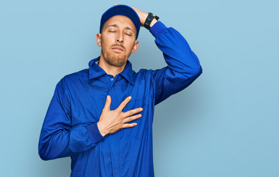 Bald man with beard wearing builder jumpsuit uniform touching forehead for illness and fever, flu and cold, virus sick