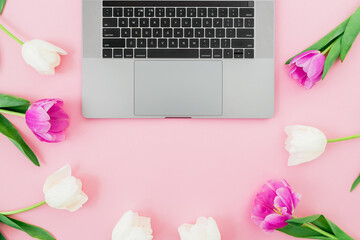 Laptop and tulips flowers on pink background. Flat lay. Distant work concept.