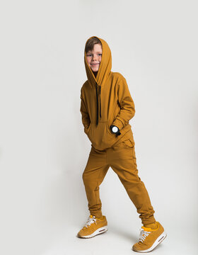 Little boy model wearing sports tracksuit with sweatshirt and pants. Portrait isolated on gray background. Male child posing for camera with hands in pocket. Autumn spring sport children fashion