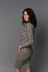 Beautiful adult woman with perfect makeup wearing a checkered dress on the grey background