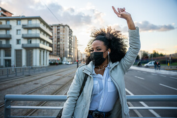 Portrait of a young woman in the evening at sunset in the city wearing protective face mask during global pandemic from Covid-19 Coronavirus dancing listening to music with earphones from smartphone