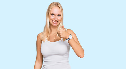 Young blonde girl wearing casual style with sleeveless shirt doing happy thumbs up gesture with...