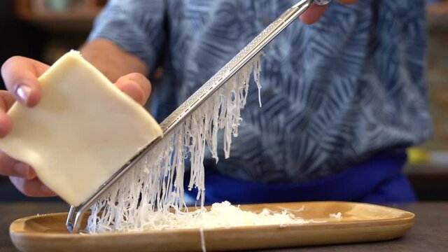 man rubs cheese on grater at home in the kitchen, hands close-up