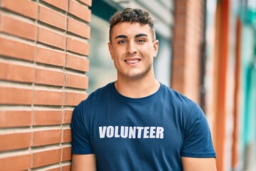 Young hispanic volunteer man smiling happy standing at the city.