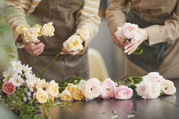 Close up of two female florists arranging roses and peonies while creating floral compositions in...