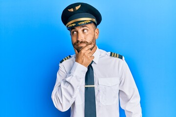 Handsome man with beard wearing airplane pilot uniform with hand on chin thinking about question, pensive expression. smiling with thoughtful face. doubt concept. © Krakenimages.com