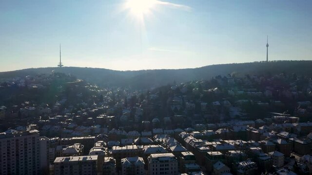 Aerial view fof beautiful city skyline with TV Tower, Telecommunication Tower, buildings and mountains covered in snow during winter in Stuttgart, Germany flying backwards.
