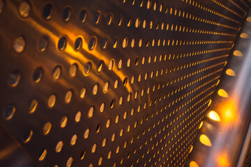 Closeup of abstract pattern background of stainless chrome metal sheet grille wall with circle holes with orange sun light pass through it.
