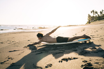 Shirtless surfer on surfboard training on sandy seashore