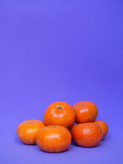 Group of mandarins fruit on a purple background. Vibrant colorful summer wallpaper with copy space....