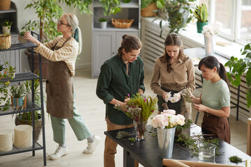 High angle view at diverse group of young florists creating floral compositions during workshop...