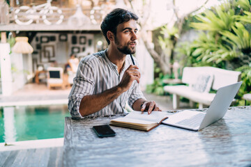 Thoughtful ethnic man with laptop and notebook