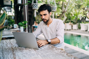 Concentrated man working on laptop on resort terrace