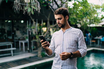 Serious young businessman using smartphone during summer vacation in tropical country