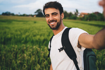 Fototapeta premium Smiling man holding camera and taking selfie on grassland