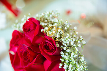 Red ribbon . Red engagement flowers on white table . Bride and groom with Engagement gold rings put on the red wedding bouquet . Red engagement bouquet .