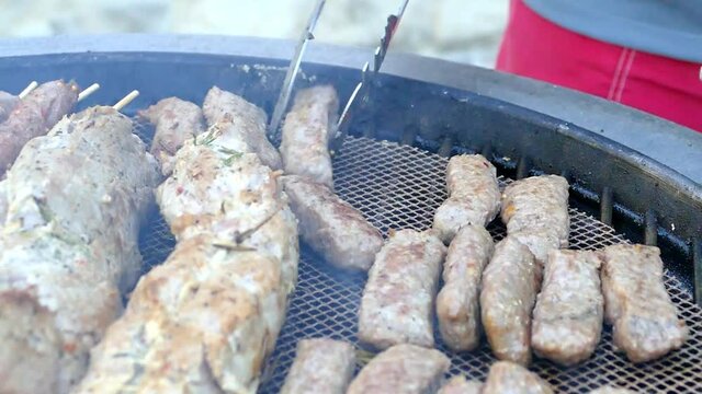 Slow motion Man turns delicious homemade Cevapcici with Barbecue tongs on a Charcoal grill, Croatia