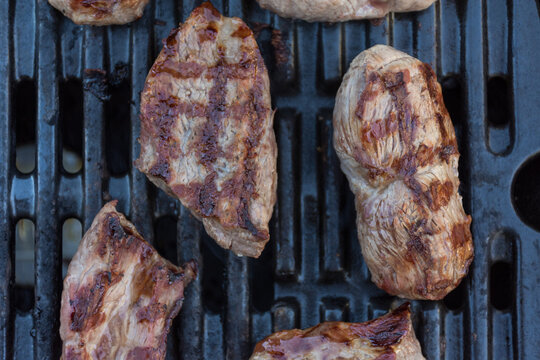 Close up of meat cooking on a barbeque grill with a spatula
