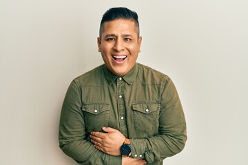 Fototapeta premium Young latin man wearing casual clothes smiling and laughing hard out loud because funny crazy joke with hands on body.