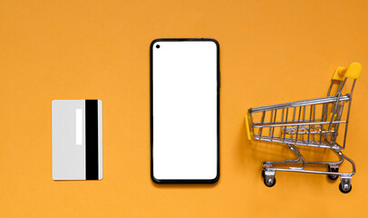 Shopping with phone, gray credit card and mini shopping trolley on orange background. App concept for online shopping, home delivery, discounts, black friday. top view. Flat lay. copy space for text