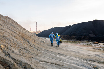 Two young contemporary ecologists in protective workwear moving along hill while investigating...