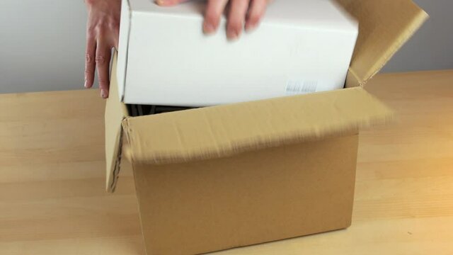 A small white box being packed into cardboard delivery box, with bubble wrap and box sealed ready for dispatch.