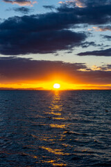 scenic and colorful sunset over the ocean with shimmering light on the waves and silhouette of mountains on the shore behind