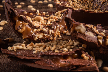 Stuffed chocolate easter egg with peanut and caramel on a wooden table with lots of peanuts around. Cracked. Close up.