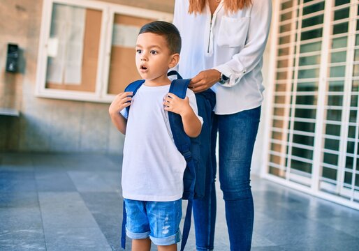 Adorable latin student boy and mom at school. Mother preparing kid putting up backpack.